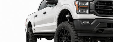 Image of a white lifted truck with large tires.