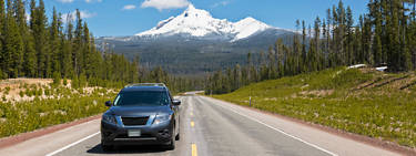 An image of a vehicle on a road trip with the road and mountains and grass in the background.