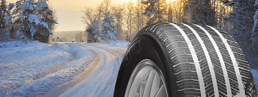 An image of an all-season tire on the right and a snowy road through a snow covered forest in the background.
