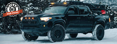 An image of a truck driving with snow tires through a snow covered road with the words 'Best snow tires for trucks: Tires: Our Picks' on the left.