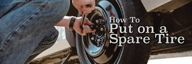 a person crouched down in the process of installing a spare tire on a car