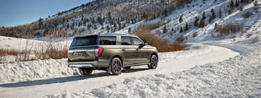 An image of a vehicle driving up a snowy road with snowy trees in the background.
