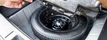 An image of a person lifting the back floorboard of their trunk to find a spare tire.