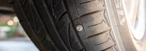 Parked car view of a tire with a nail in the tread.