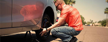 Man in orange shirt mounting his spare tire on his car