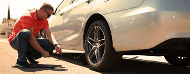Man in orange shirt preparing to loosen the lug nuts on his silver car