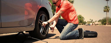 Man in orange shirt loosening his lug nuts on his silver car