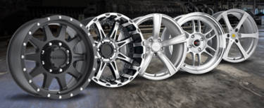 5 wheels of various designs and differently numbered bolt patterns sitting in a room with a wooden floor