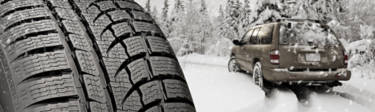 Snow tire with sipes in front of a car driving down a snowy road
