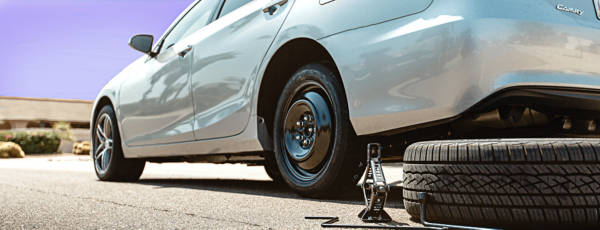 Rear of white car in the process of getting a spare tire installed