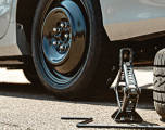 Spare Tire freshly applied to a vehicle next to a scissor jack and a flat tire