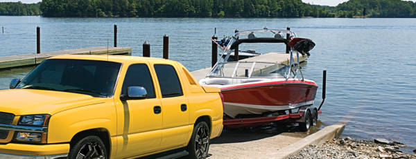 Boat trailer hitched to a yellow pickup truck, being backed into a lake featuring aftermarket wheels.
