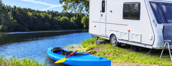 A white camper with 13 inch tires parked by a river with a kayak in the foreground. 
