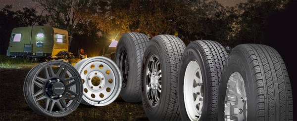 Assortment of trailer wheels and tires sitting in the woods with a camper in the background at night