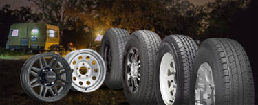 Assortment of trailer wheels and tires sitting in the woods with a camper in the background
