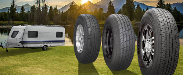 Camper trailer on green grass near a lake with an assortment of trailer tires and wheels