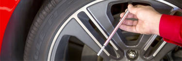 Close up of hand using tire gauge to check tire air pressure.