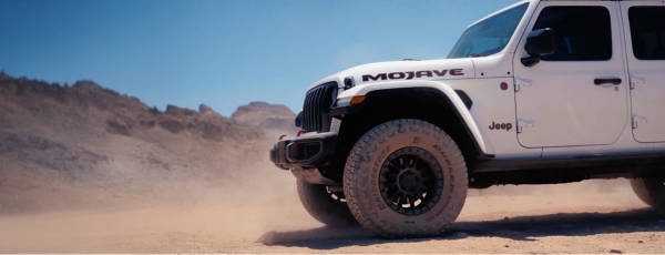 Jeep Gladiator with Bridgestone Dueler Maverick A/T tires rolling through a dusty desert road.